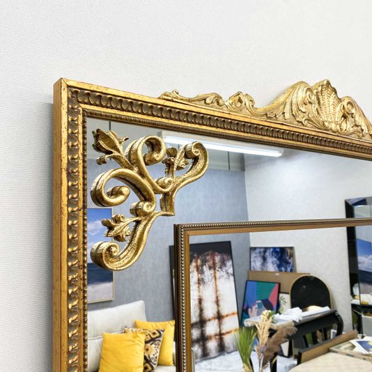 Detalhe do acabamento dourado brilhante do espelho clássico com apliques folheados.